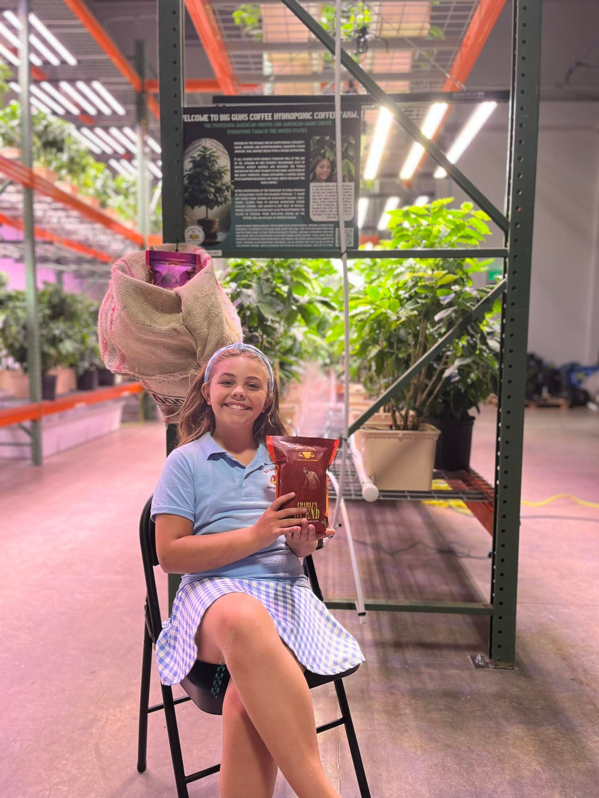 Big Guns Coffee co-founder Charli holding her Charli's Blend bag beside indoor coffee plants; brand-story photo